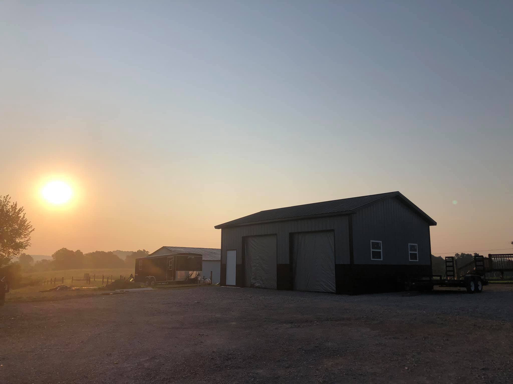 Two large garages and a trailer sit under a hazy sky at sunrise.