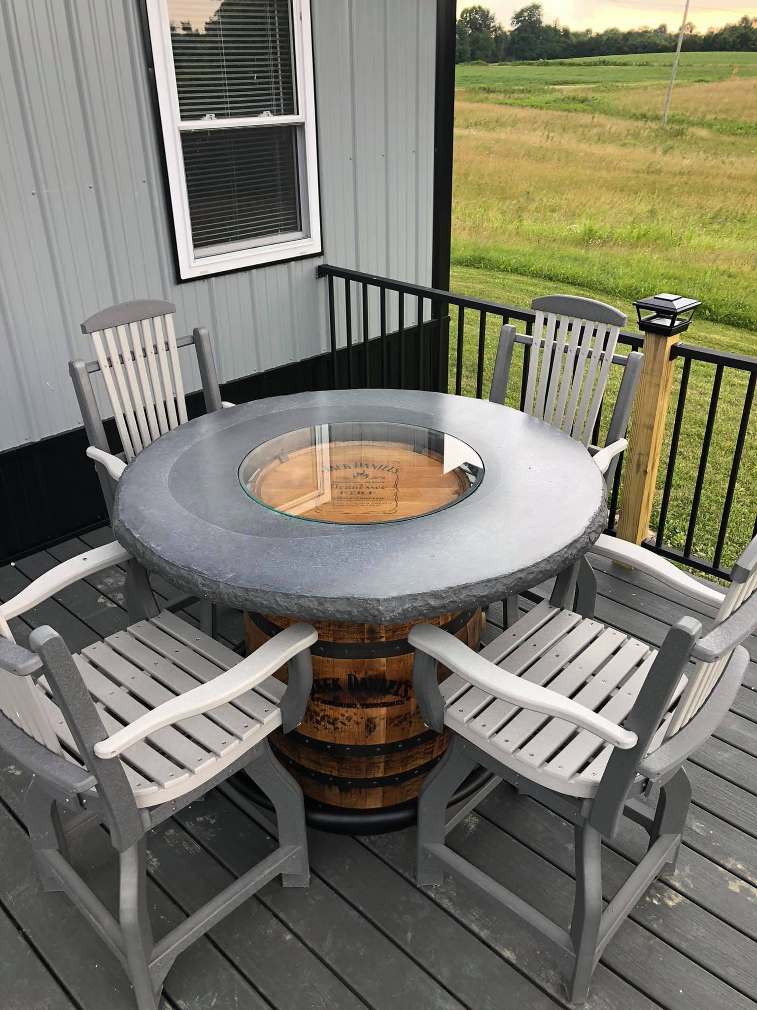 A unique whiskey barrel table with chairs on a wooden deck overlooking a field.
