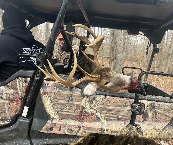 Hunter kneeling beside a harvested Kentucky whitetail buck on the property.