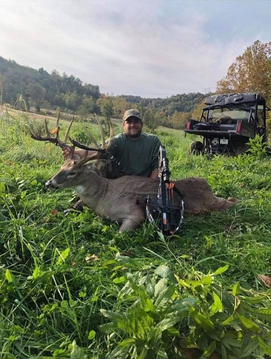 Hunter with a large buck and crossbow in grassy Kentucky hills.