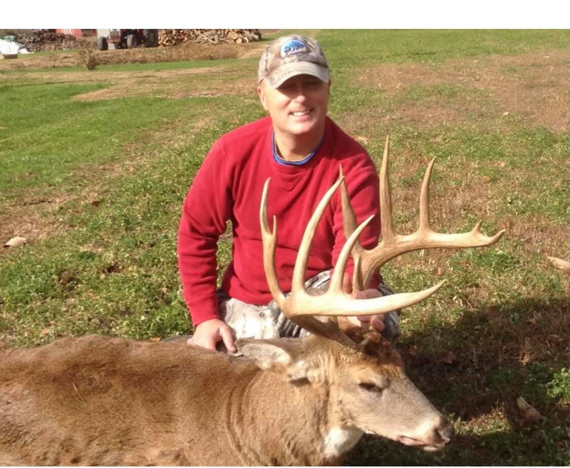 Hunter proudly displays large buck with impressive rack in grassy field.