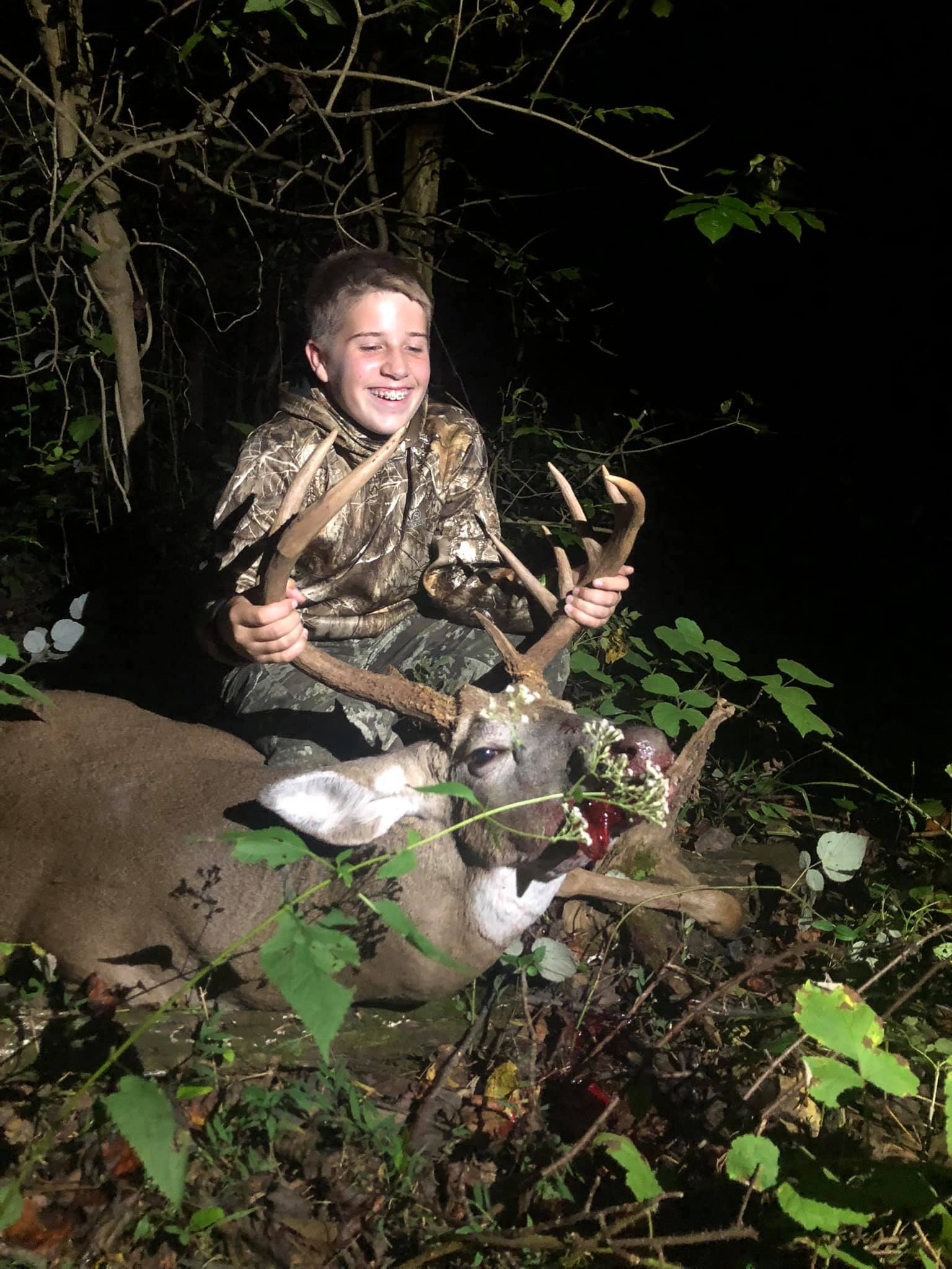 A young hunter smiles proudly while holding the antlers of a harvested buck.