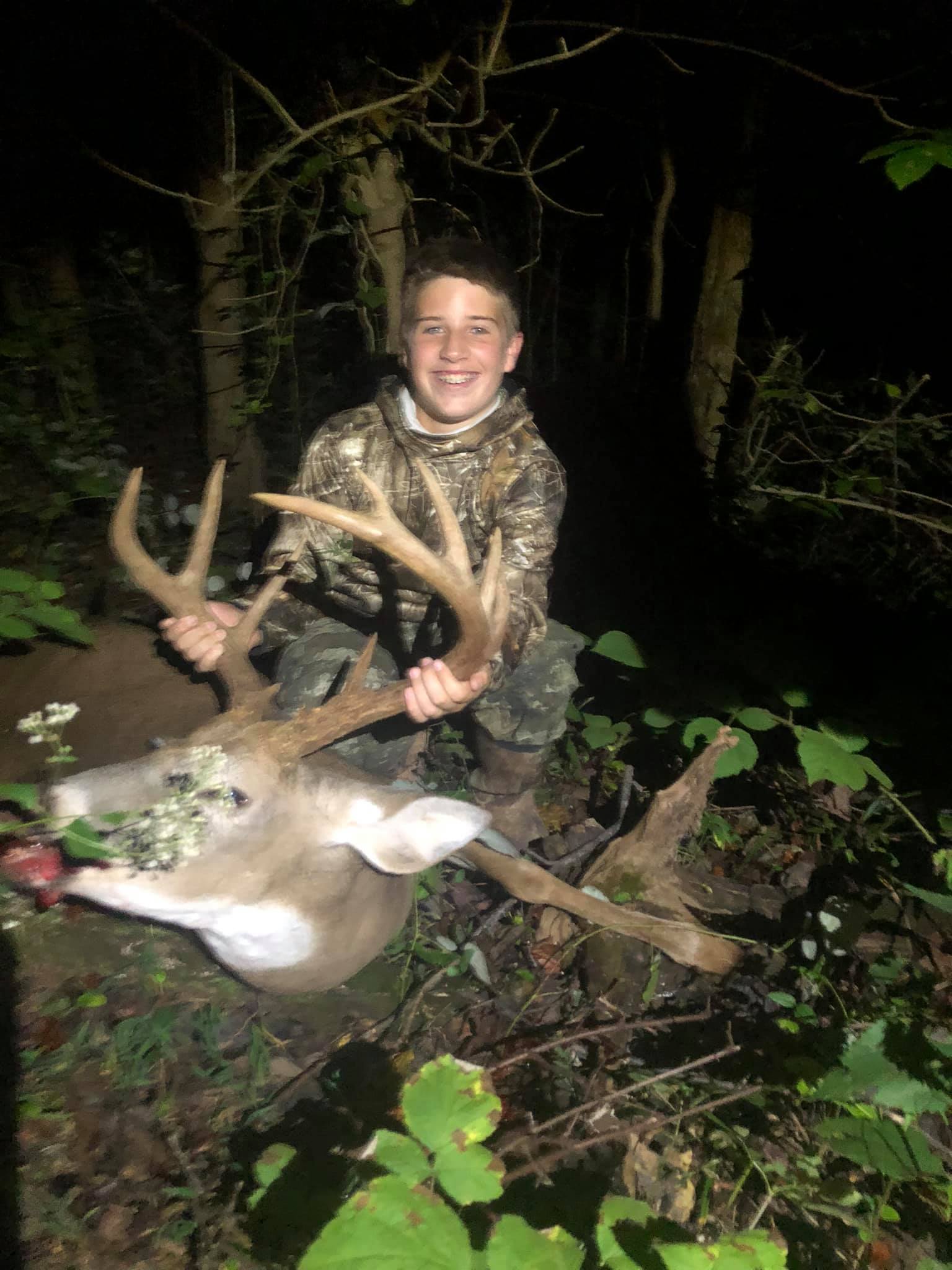 A young hunter proudly displays a large buck on a night hunt.