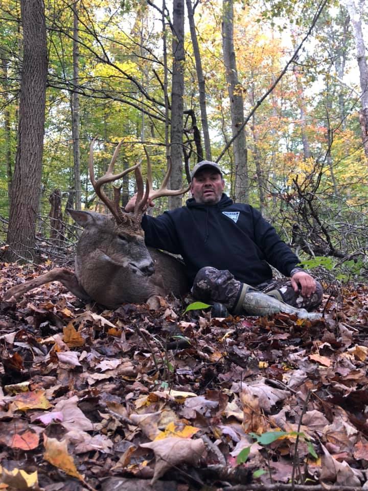 Man with a large buck in a forest during fall.