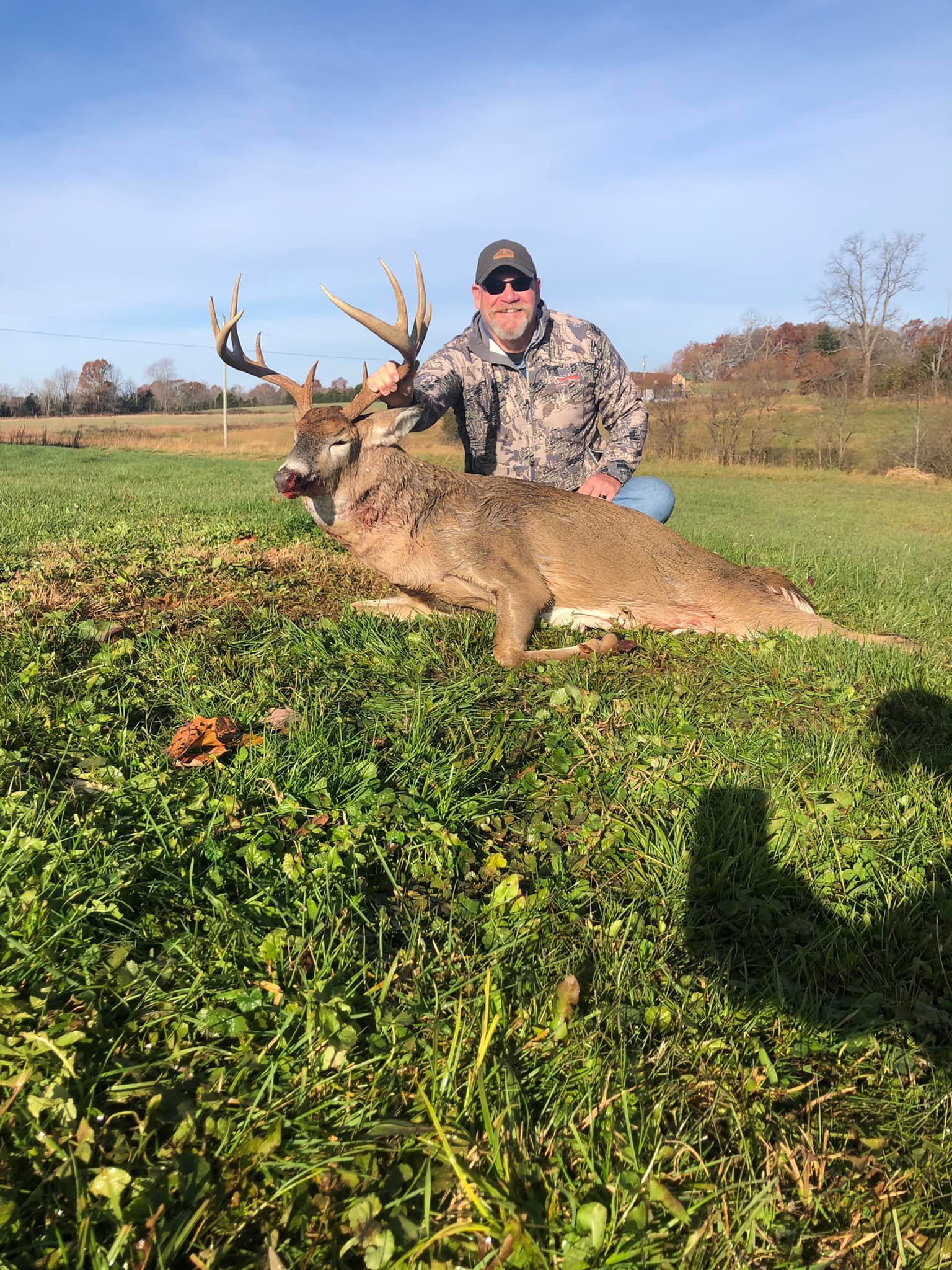 Hunter kneels behind a downed buck with impressive antlers in a grassy field.