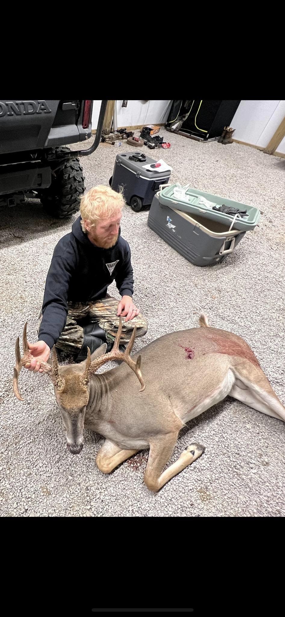 A young man poses with a harvested whitetail buck beside a utility vehicle.