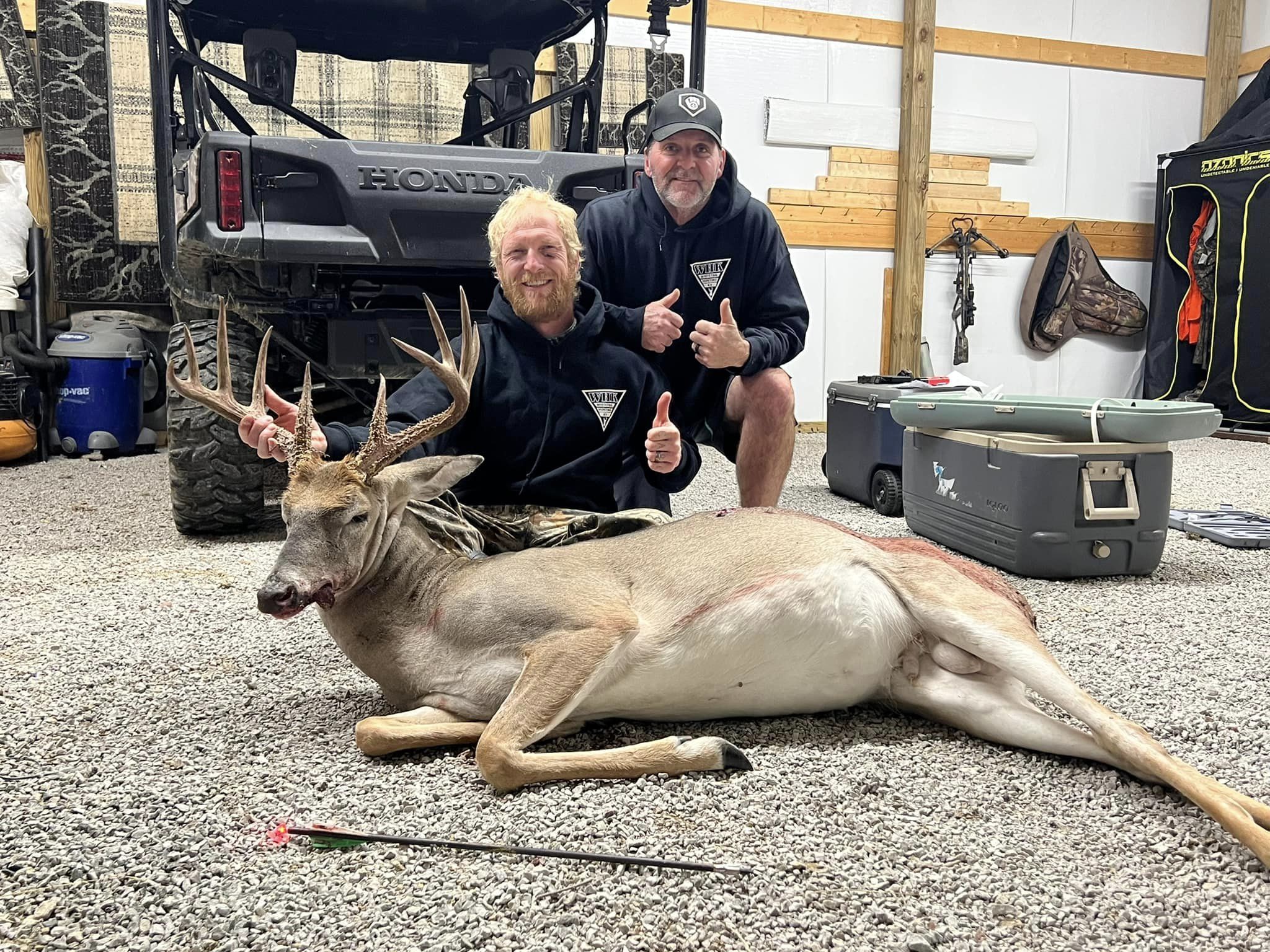 Two hunters give thumbs up next to a harvested whitetail buck.