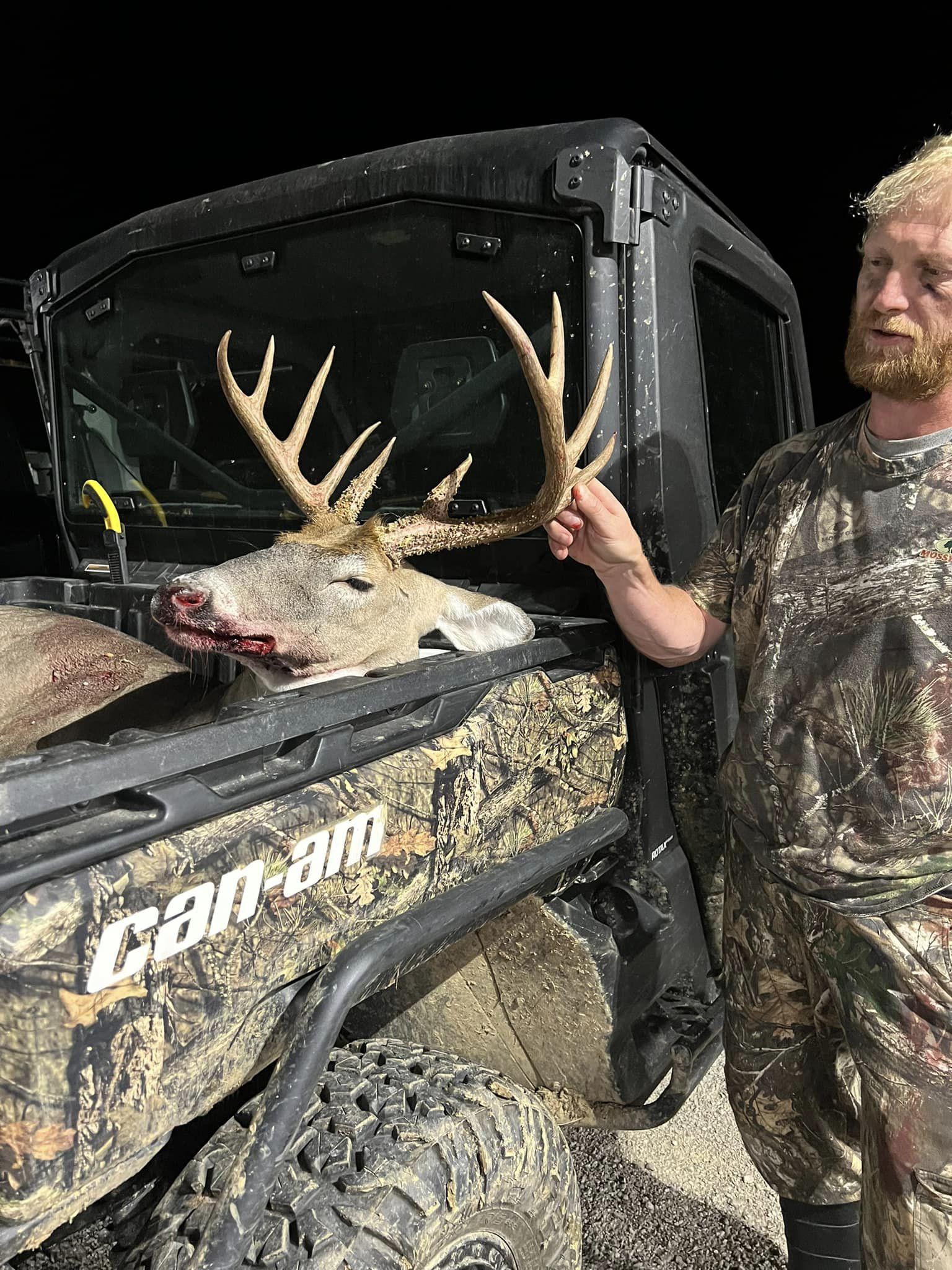 Hunter with harvested whitetail buck in the back of a Can-am ATV at night.