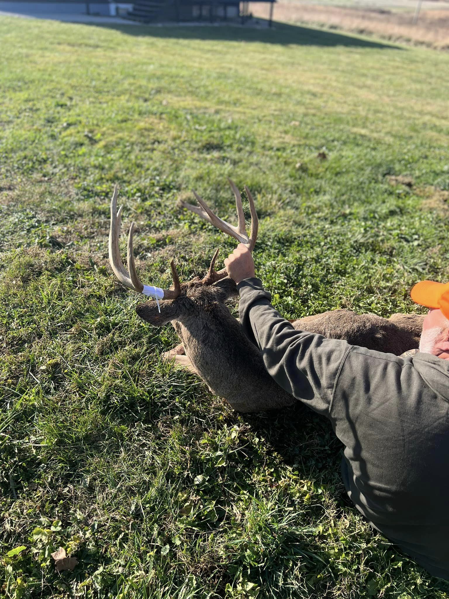 A hunter displays a harvested whitetail buck with antlers wrapped in white tape.