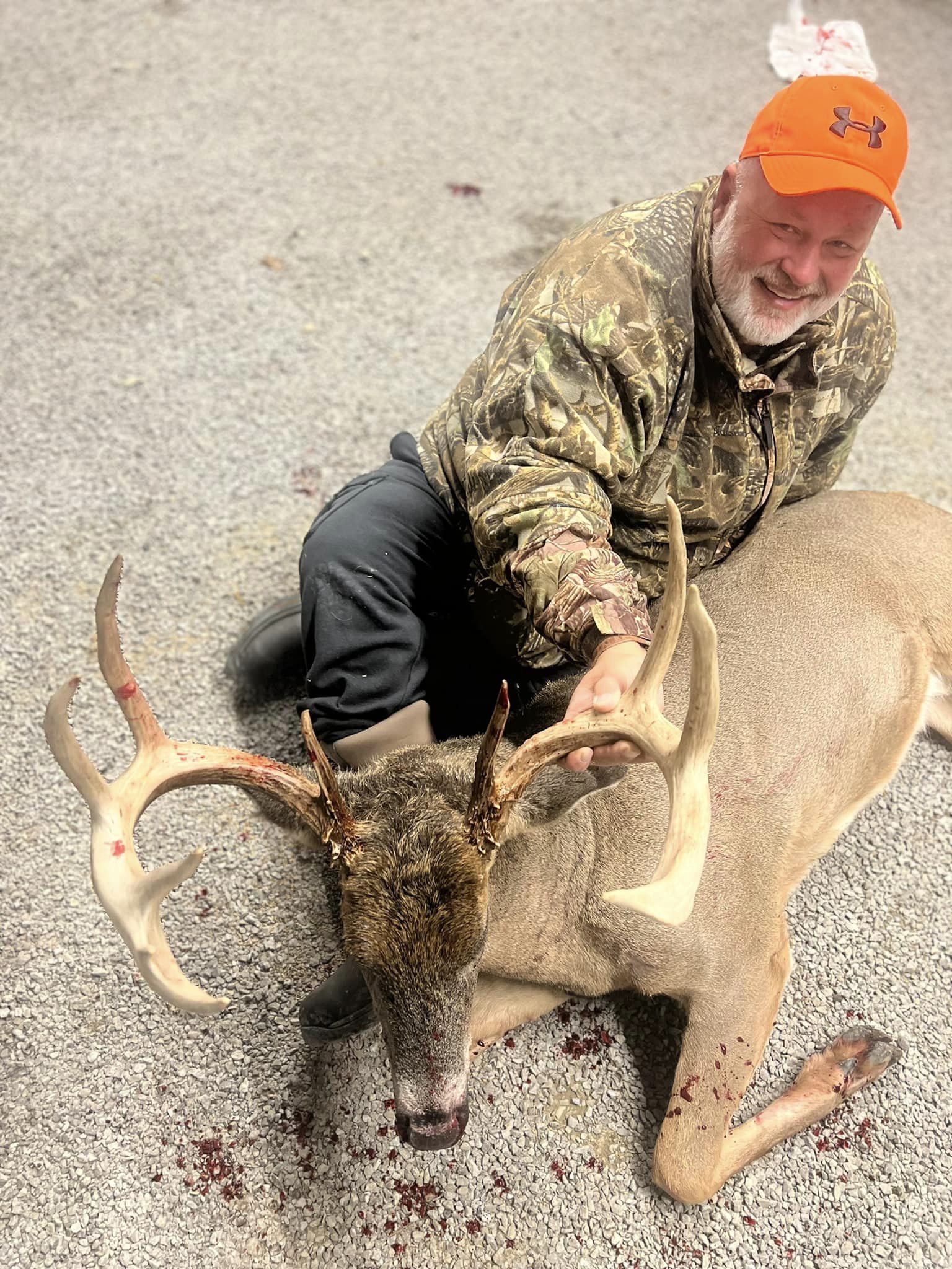 Hunter kneeling beside a whitetail buck with large antlers.