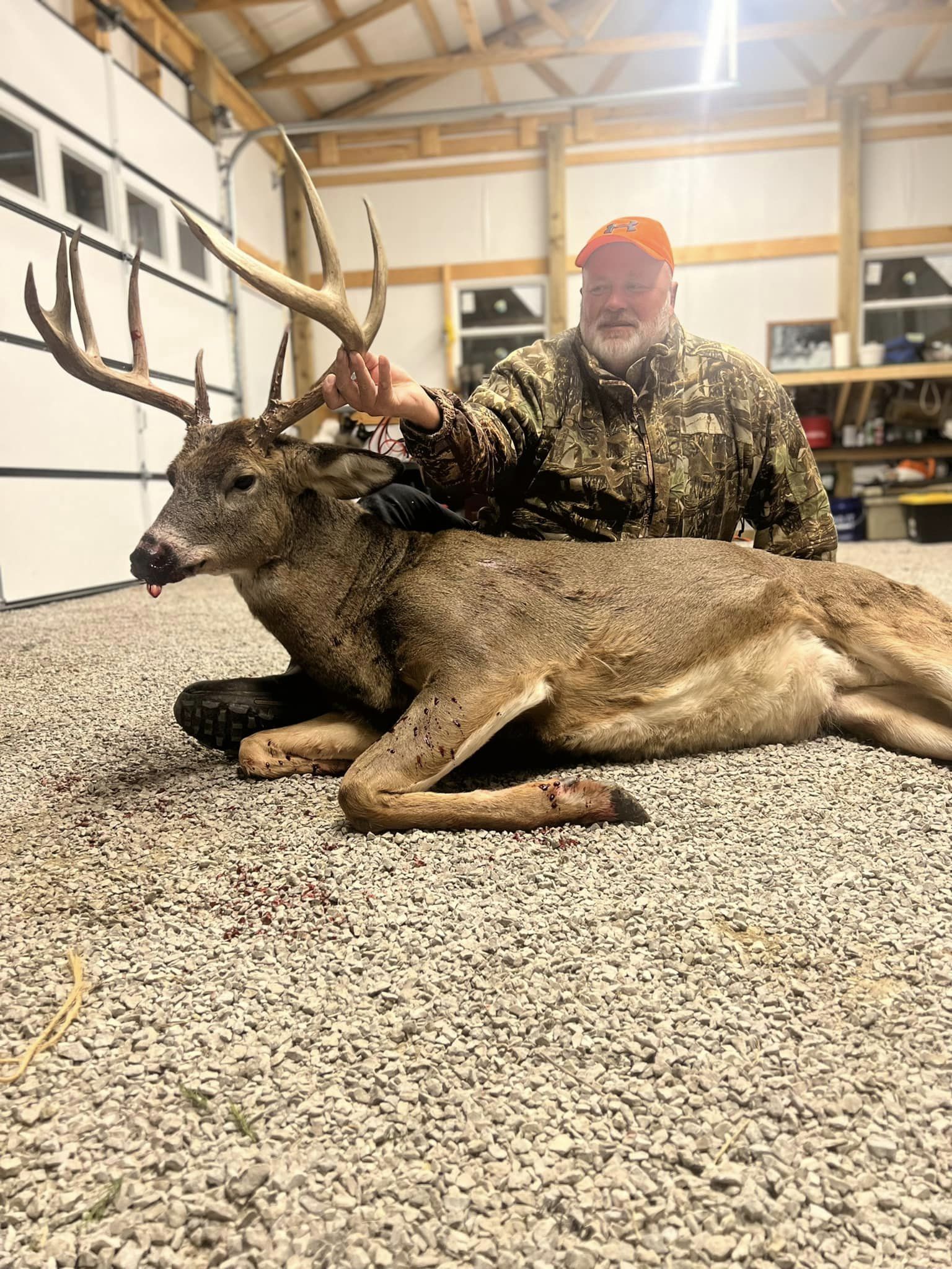 Hunter with a large antlered buck in a garage.