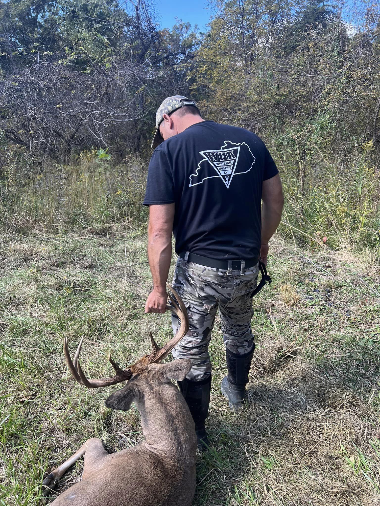 Hunter displays a buck with antlers in velvet in a grassy field.