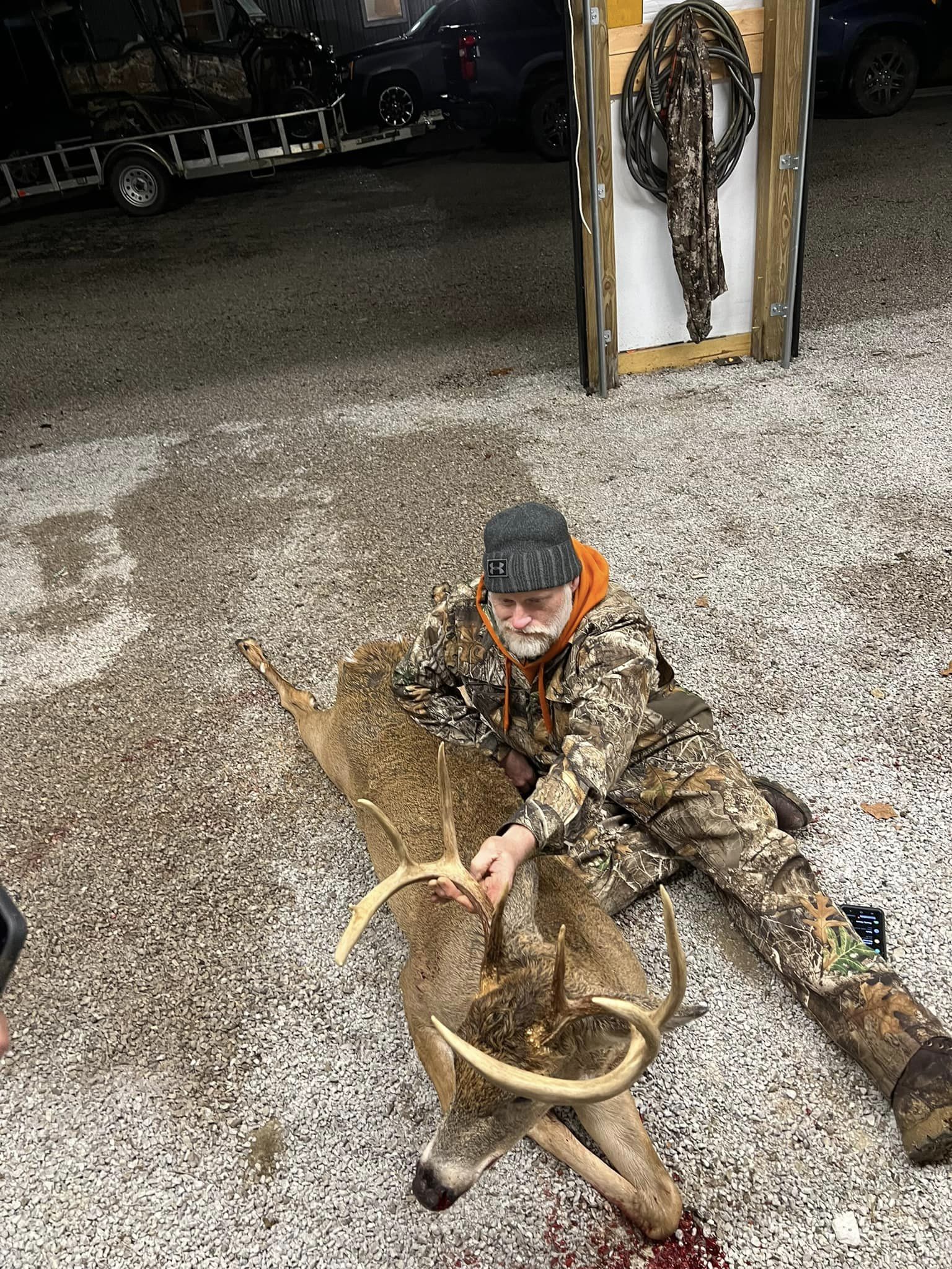 Hunter with a whitetail buck on a gravel lot.