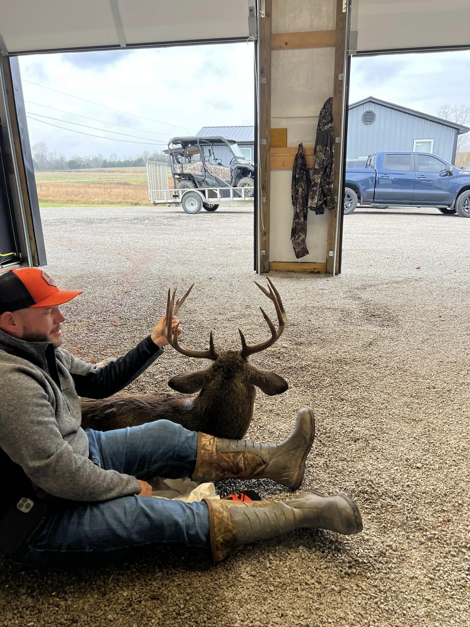 Hunter examines a large buck's antlers in front of a garage.