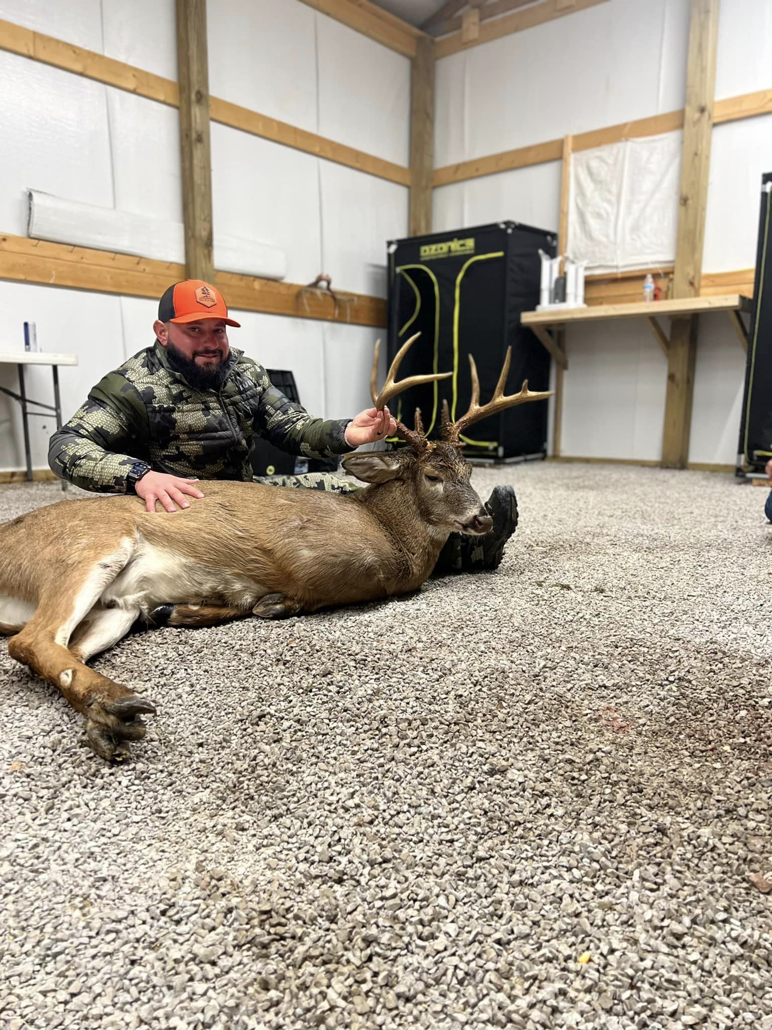 Hunter poses with a mature Kentucky whitetail buck in a gravel-floored building.